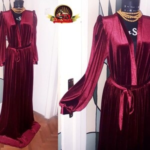 May include: A long, burgundy velvet robe with a V-neckline and long sleeves. The robe has a sash tie at the waist and a pleated skirt.