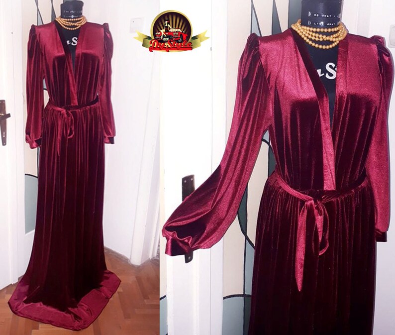 May include: A long, burgundy velvet robe with a V-neckline and long sleeves. The robe has a sash tie at the waist and a pleated skirt.