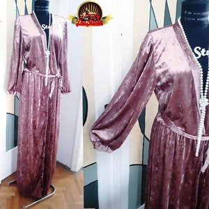 May include: A long, dusty rose velvet robe with a V-neckline and long sleeves. The robe has a tie at the waist and is made of a soft, luxurious fabric.