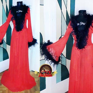 Puede incluir: Una larga bata roja transparente con ribete de plumas negras alrededor del cuello, las mangas y la faja. La bata est&aacute; hecha de una tela ligera y fluida.
