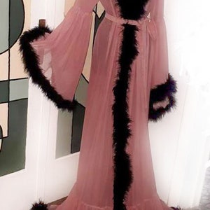 May include: A pink sheer robe with black feather trim. The robe has a long, flowing silhouette and a tie at the waist.