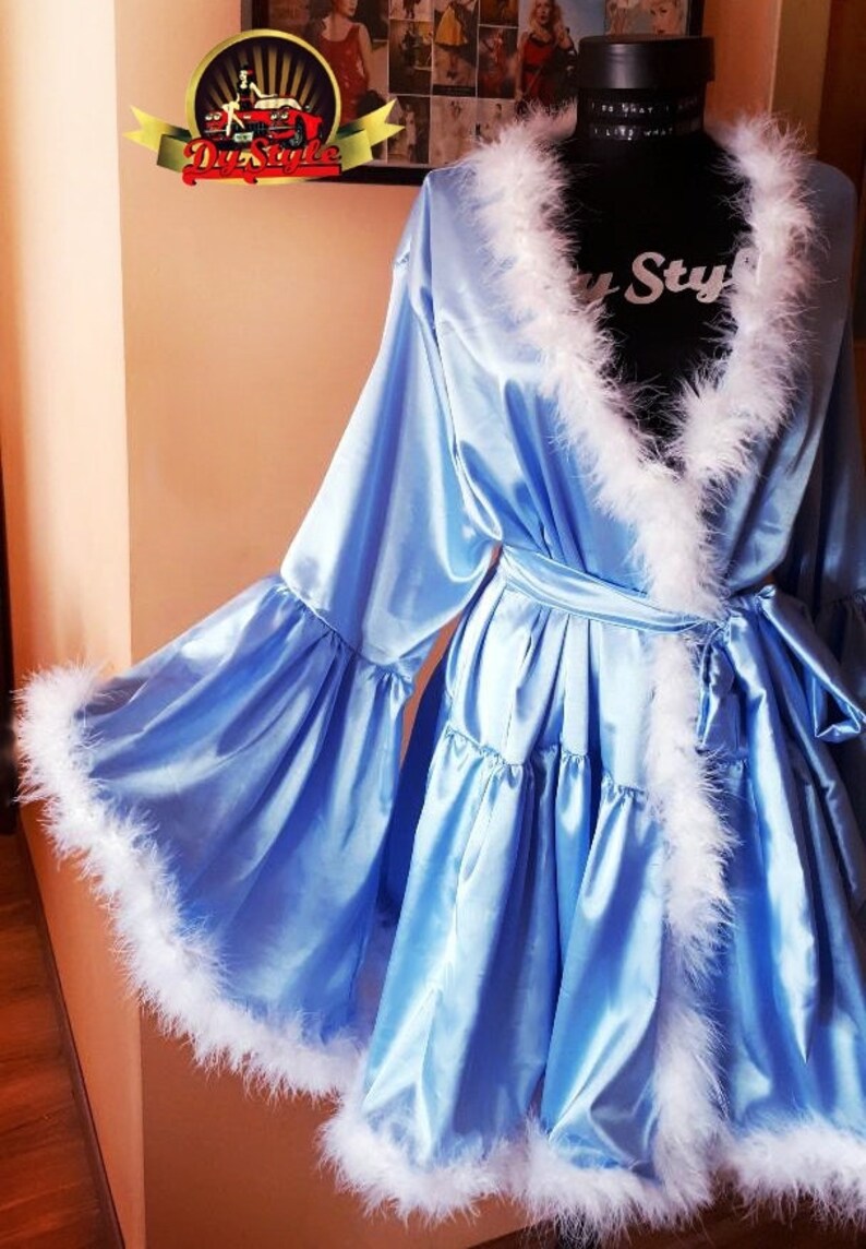 May include: A light blue satin robe with white feather trim around the neckline, sleeves, and hem. The robe has a tie belt and a ruffled skirt.