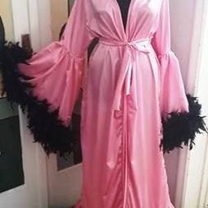 Puede incluir: Una larga bata de satén rosa con ribete de plumas negras alrededor de las mangas y el dobladillo. La bata tiene un lazo en la cintura y una falda larga y fluida.