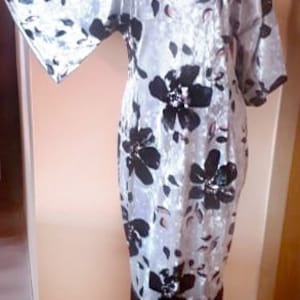 Puede incluir: Un vestido de terciopelo blanco con estampado floral negro y ribete de flecos. El vestido tiene un escote redondo y mangas cortas.