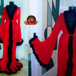 Puede incluir: Una bata roja de gasa transparente con ribete de plumas negras alrededor del cuello, las mangas y el dobladillo. La bata tiene un cinturón de lazo y una silueta larga y fluida.