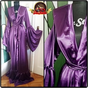 Puede incluir: Una larga bata de satén morado con cuello en V y mangas largas. La bata tiene un cinturón de lazo y un dobladillo con volantes.