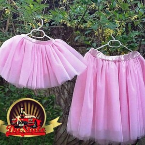 May include: Two pink tulle skirts hanging on hangers. The skirts are layered and have a satin waistband.