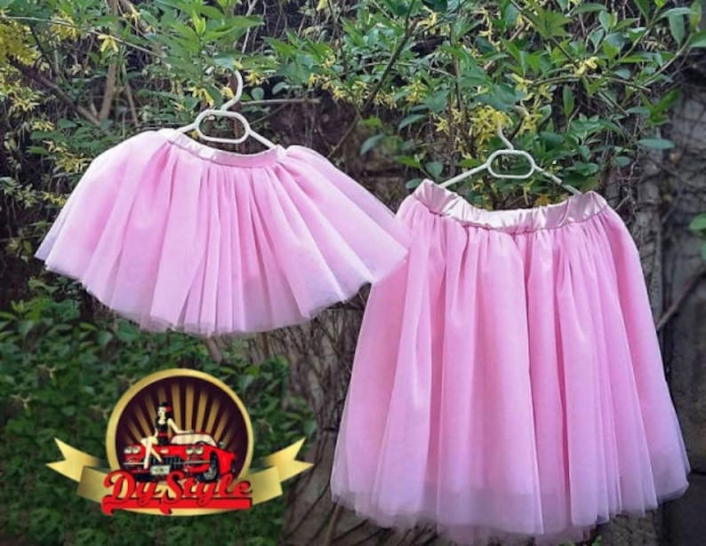 May include: Two pink tulle skirts hanging on hangers. The skirts are layered and have a satin waistband.