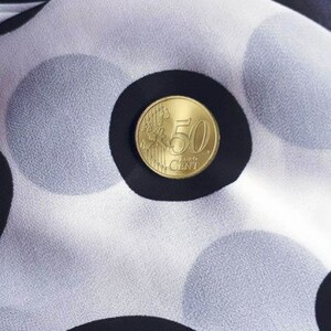 May include: A 50 cent Euro coin on a white fabric with black polka dots.