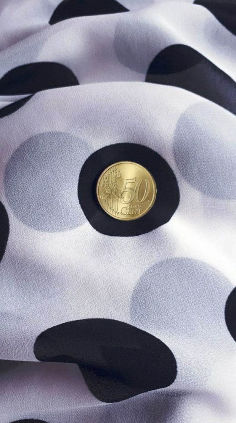 May include: A 50 cent Euro coin on a white fabric with black polka dots.