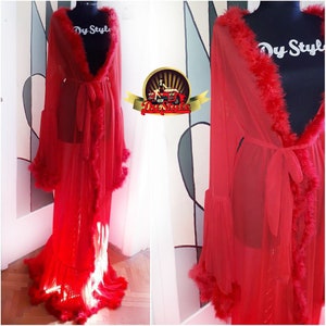 Puede incluir: Una bata roja de encaje transparente con un ribete de plumas alrededor del cuello, las mangas y el dobladillo. La bata tiene un lazo en la cintura y está hecha de una tela ligera.