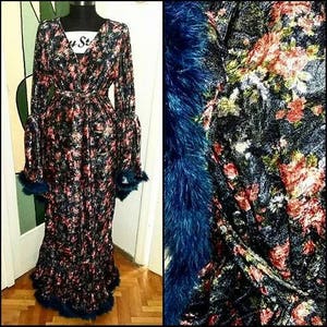 Puede incluir: Una larga bata de terciopelo negro con estampado floral y ribete de plumas azules. La bata tiene cierre de envoltura y mangas largas.