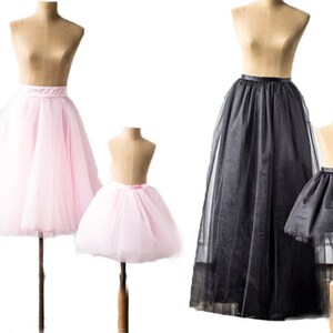 May include: Two tulle skirts, one pink and one black, are displayed on mannequins. The skirts are full and flowy, with a satin waistband. The pink skirt is shorter than the black skirt.