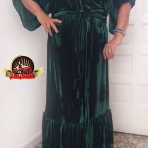 Puede incluir: Una larga bata de terciopelo verde oscuro con estilo de envoltura y un dobladillo con volantes. La bata tiene un cuello en V y un cinturón de lazo.