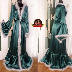 Puede incluir: Una larga bata de satén verde con ribete de plumas blancas. La bata tiene cuello chal, mangas largas y cinturón de lazo. La bata tiene un dobladillo con volantes.