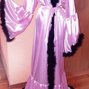 May include: A long pink satin robe with black feather trim. The robe has a ruffled hem and a tie belt. The robe is on a mannequin.