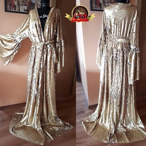 Könnte beinhalten: Eine lange, goldene Paillettenrobe mit V-Ausschnitt und langen Ärmeln. Die Robe hat einen Bindegürtel in der Taille und einen fließenden Rock.