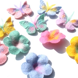 Può includere: Assortimento di fiori e farfalle in feltro di colori pastello. I fiori sono in tonalità di rosa, giallo, blu e verde. Le farfalle sono in tonalità di rosa, giallo e blu.