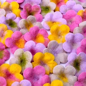 Könnte beinhalten: Eine Sammlung von Filzblumenverzierungen in den Farben Rosa, Gelb, Grün und Lila. Die Blumen haben alle fünf Blütenblätter und eine leicht flauschige Textur.