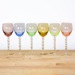 Pode incluir: Um conjunto de seis taças com bojos coloridos nos tons rosa, azul, verde claro, amarelo, verde lima e pêssego. Cada taça possui uma haste transparente com um padrão espiral torcido e uma base circular, dispostas em uma fila horizontal.