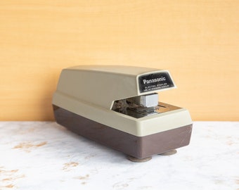 Puede incluir: Una grapadora eléctrica beige y marrón con el texto "Panasonic Electric Stapler Use HP Standard Staples" en la parte superior.