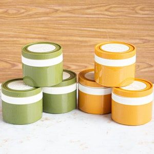 Op de afbeelding: Zes vintage opbergcontainers, drie groen en drie geel, gestapeld in twee stapels van drie. De containers hebben witte deksels en zijn gemaakt van plastic.