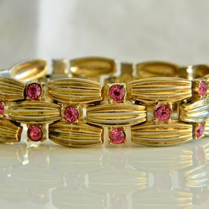 May include: A gold tone bracelet with a linked design and pink rhinestones.