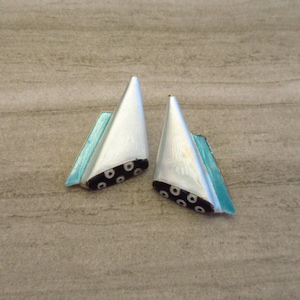 May include: A pair of silver earrings with a geometric design. The earrings are shaped like triangles with a blue enamel base and black and white dots.
