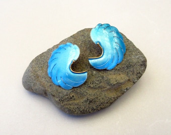 May include: A pair of blue enamel earrings shaped like a crescent moon with a gold accent. The earrings are sitting on a gray rock.