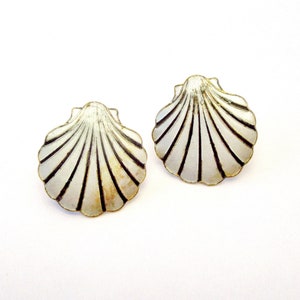May include: A pair of silver shell-shaped earrings. The earrings are a simple design with a white enamel finish and black lines.