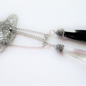 May include: A silver chain necklace with two crystal pendants. One pendant is clear and the other is black. Both pendants have a silver and rhinestone embellishment.