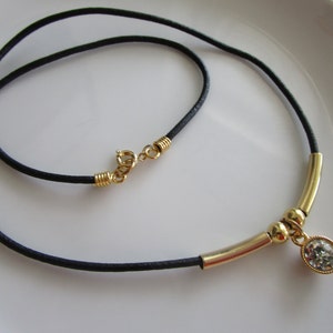 May include: A black leather cord necklace with a gold bar and a round clear crystal pendant.