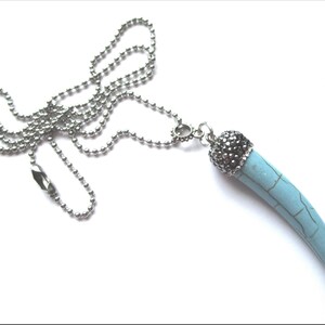 May include: A silver chain necklace with a turquoise blue pendant shaped like a tooth. The pendant is topped with a silver cap with black rhinestones.