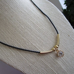 May include: A black cord necklace with gold beads and a clear crystal pendant.