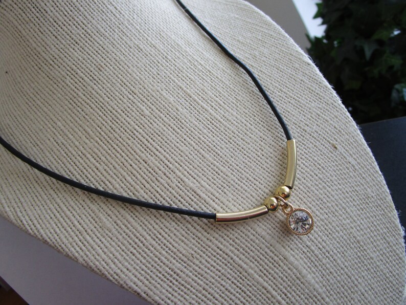 May include: A black cord necklace with gold beads and a clear crystal pendant.