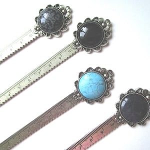 May include: Four silver metal ruler bookmarks with decorative floral accents and different coloured gemstone cabochons. The bookmarks are 10 inches long and feature a ruler on one side.