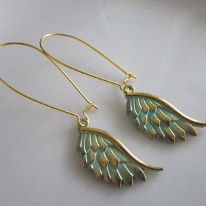 May include: A pair of gold dangle earrings with turquoise blue wings. The wings are detailed with a textured pattern.