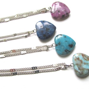 May include: Four silver chain necklaces with heart-shaped pendants. The pendants are made of different types of stone: pink, blue, turquoise, and light blue with brown streaks.
