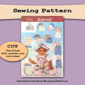 May include: A Butterick sewing pattern for baby clothes, featuring a baby in a floral outfit. The pattern includes various outfits like overalls, shorts, and tops. The text on the pattern reads "Sewing Pattern" and "CUT".