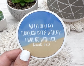 May include: A round sticker with a blue sky and sandy beach background. The sticker features the text "WHEN YOU GO THROUGH DEEP WATERS, I WILL BE WITH YOU. Isaiah 43:2".