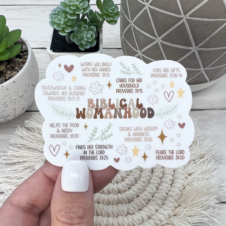 May include: A white cloud-shaped sticker with brown, beige, and green accents. The sticker features the text "Biblical Womanhood" in brown letters with a floral design. The sticker also includes several Bible verses from Proverbs 31.
