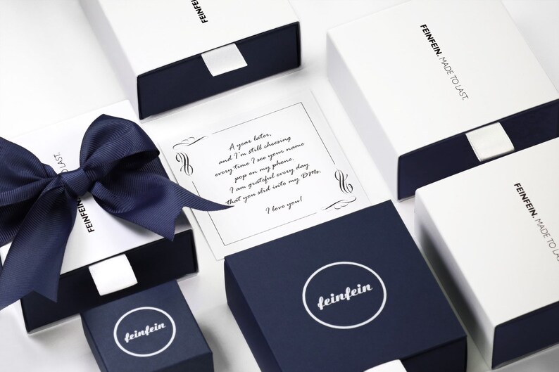 May include: A white box with a blue ribbon and a note inside that reads "A year later, and I'm still choosing every time I see your name pop on my phone. I am grateful every day that you slid into my DMs. I love you!" The box is labeled "feinfein" and "FEINFEIN. MADE TO LAST."