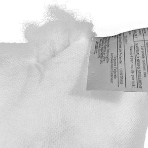 May include: Close-up of a white pillow or cushion, showing the textured fabric and fluffy filling. A tag with text in English and French is attached to the pillow. The tag includes information about the materials and manufacturing.