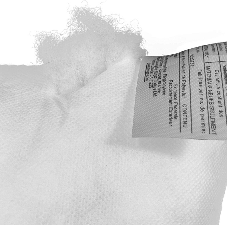May include: Close-up of a white pillow or cushion, showing the textured fabric and fluffy filling. A tag with text in English and French is attached to the pillow. The tag includes information about the materials and manufacturing.