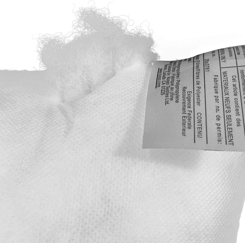 May include: Close-up of a white pillow or cushion, showing the textured fabric and fluffy filling. A tag with text in English and French is attached to the pillow. The tag includes information about the materials and manufacturing.