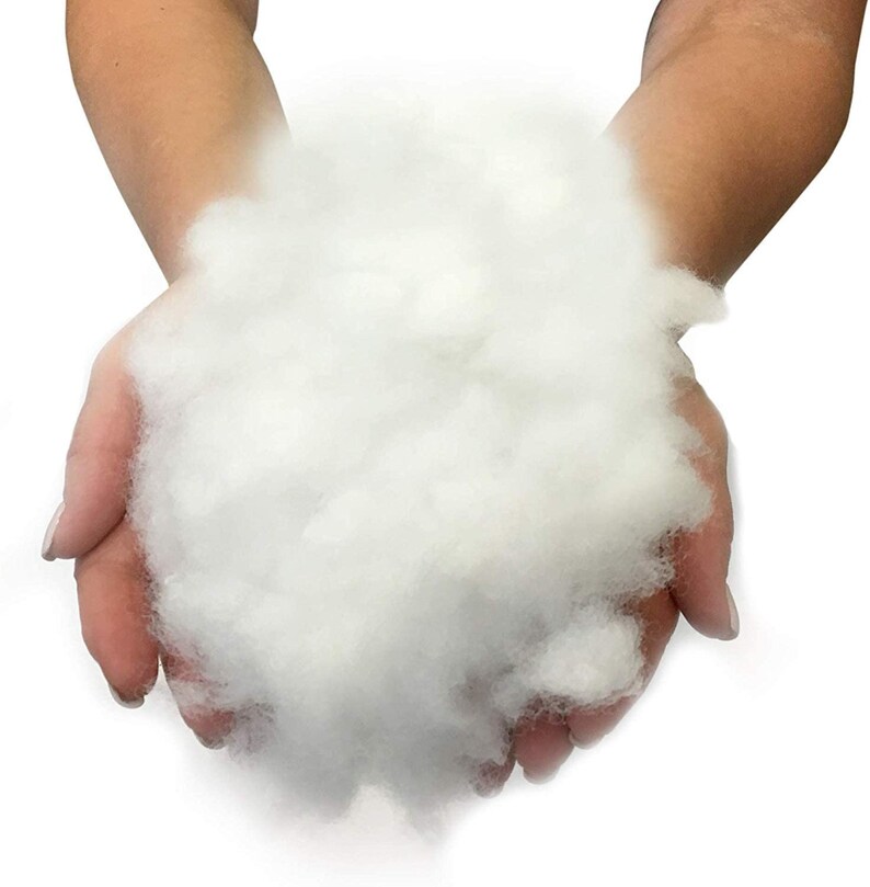 Op de afbeelding: Een close-up van een handvol zachte, witte polyester vezelvulling, ideaal voor het vullen van kussens, speelgoed of knutselprojecten. Het wolkenachtige materiaal wordt in open handen tegen een witte achtergrond gehouden.