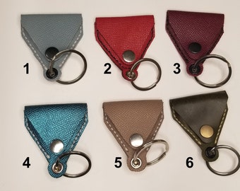 May include: Six leather keychains in different colors, including gray, red, burgundy, teal, beige, and olive green. Each keychain has a small triangle-shaped leather pouch with a snap closure and a silver key ring.
