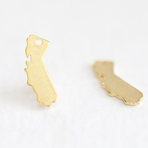 May include: A pair of gold-colored earrings shaped like the state of California. The earrings are small and delicate, and they would make a great gift for anyone who loves California.