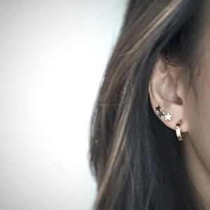 May include: A person wearing gold hoop earrings and three small gold star earrings in their left ear.