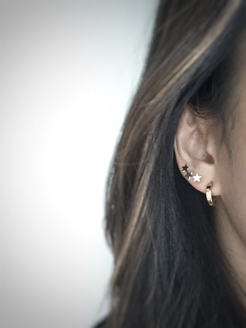 May include: A person wearing gold hoop earrings and three small gold star earrings in their left ear.